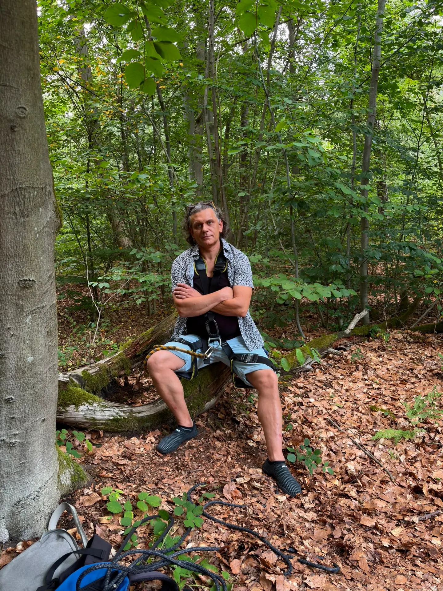 Sven Schwind sitzt ruhig mit Klettergurt und Seil auf einem umgestürzten Baumstamm im Wald